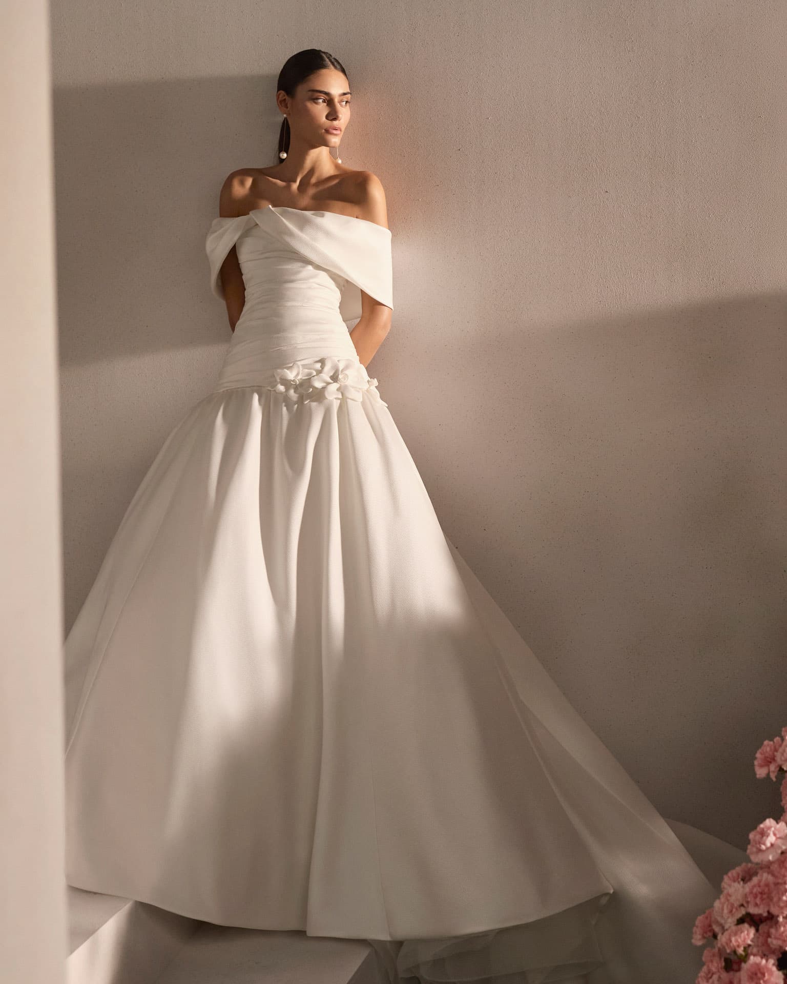 Bride in an off-the-shoulder gown against a warm plaster wall